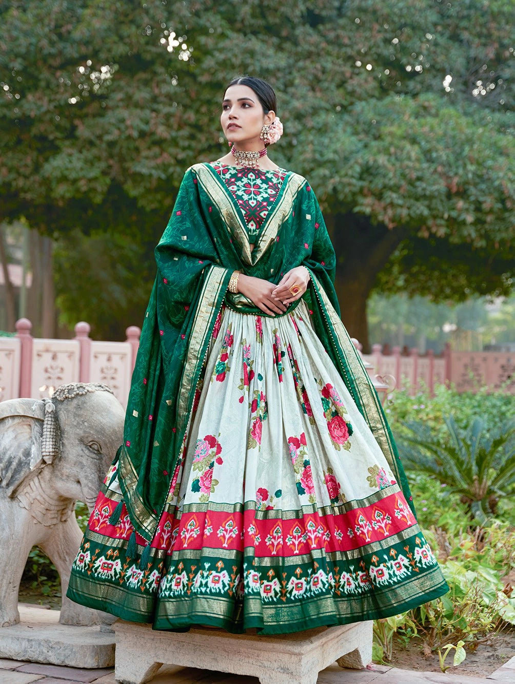 Woman in traditional green and white embroidered outfit standing outdoors with trees in the background