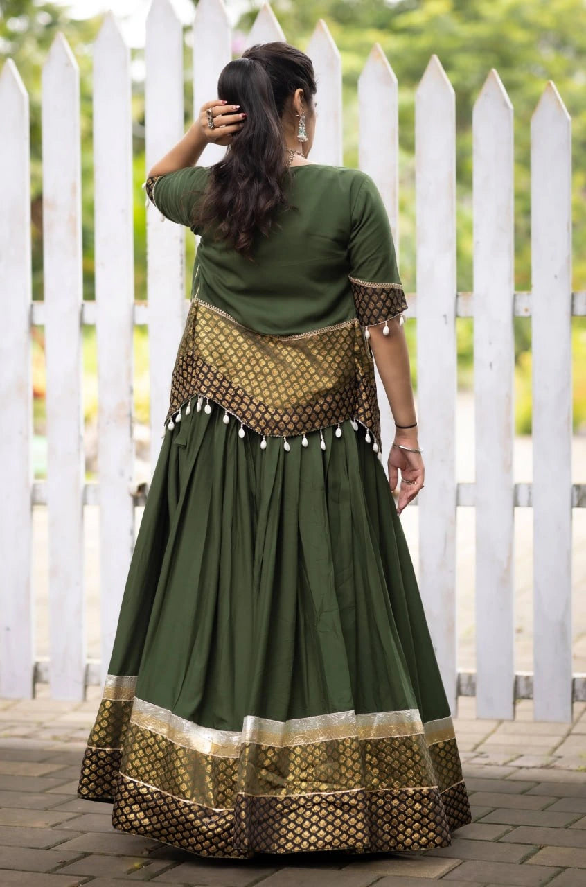 Woman wearing a green and gold traditional outfit with a white picket fence in the background
