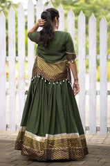 Woman wearing a green and gold traditional outfit with a white picket fence in the background
