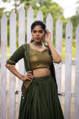 Woman in a green traditional outfit standing in front of a white picket fence.