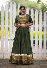 Woman in a green traditional outfit standing in front of a white picket fence.