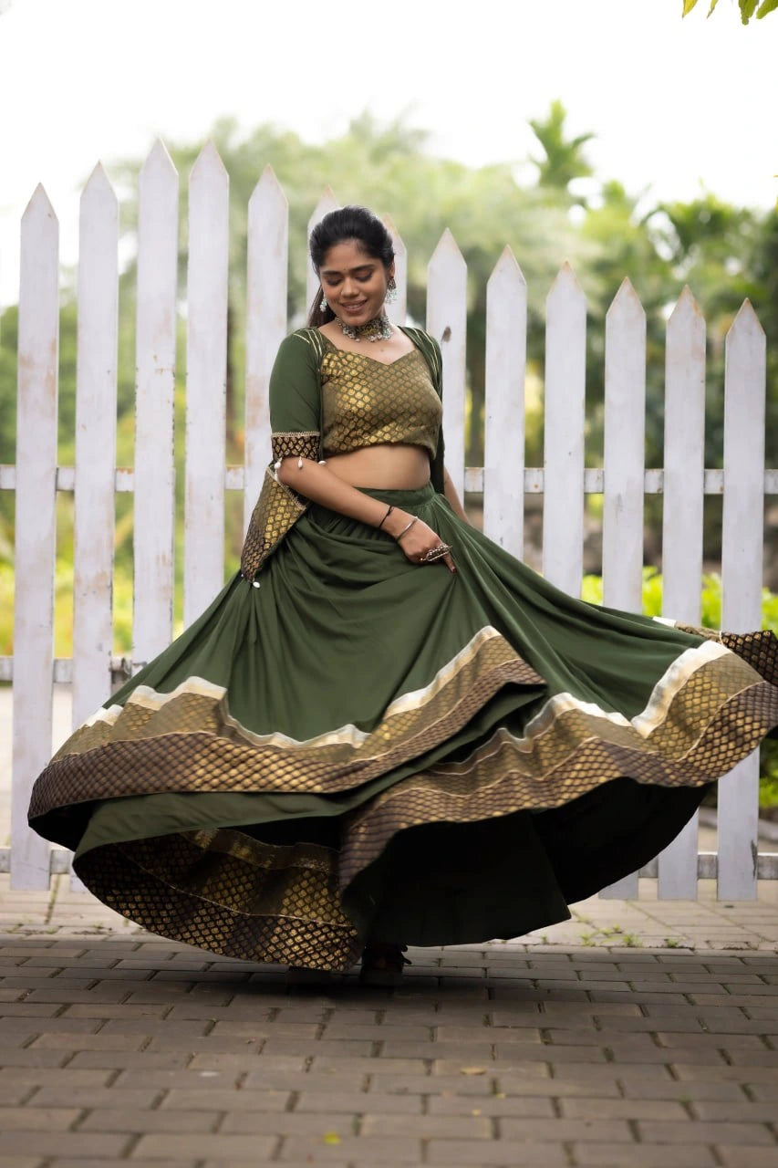 Woman in a green and gold traditional outfit dancing outdoors with a white picket fence in the background.
