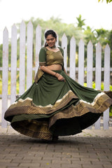 Woman in a green and gold traditional outfit dancing outdoors with a white picket fence in the background.