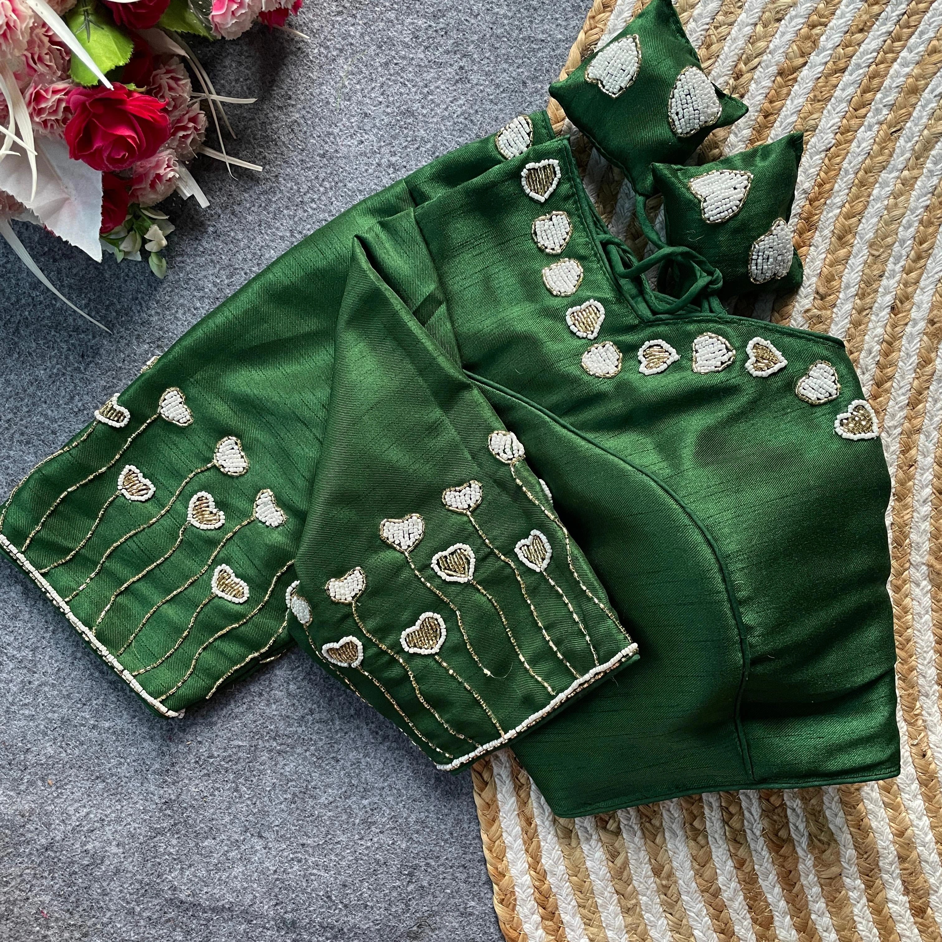 Green embroidered blouse with matching saree on a textured surface with flowers in the background