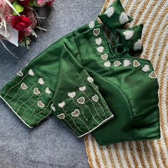 Green embroidered blouse with matching saree on a textured surface with flowers in the background