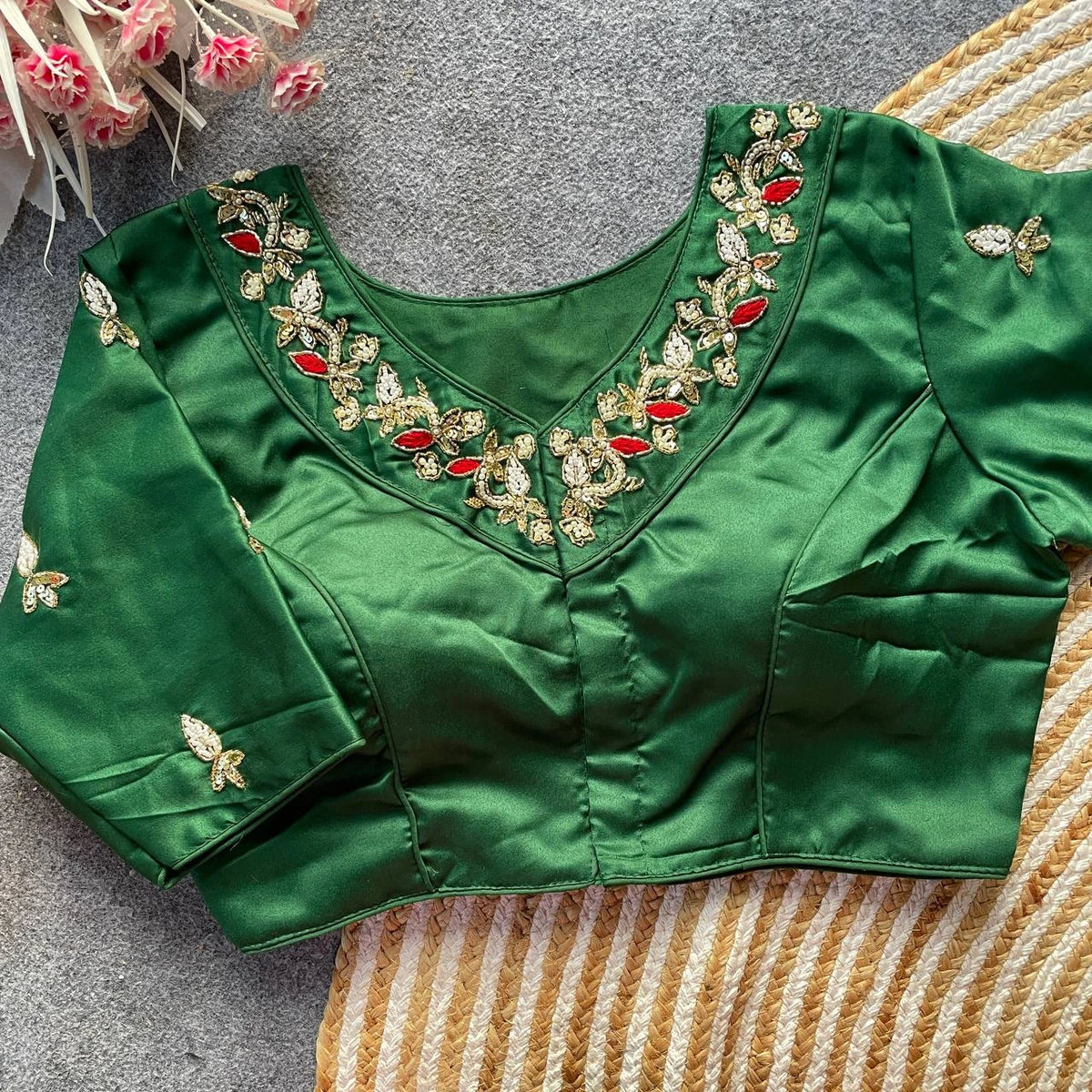 Green blouse with intricate gold and red embroidery on a textured surface.