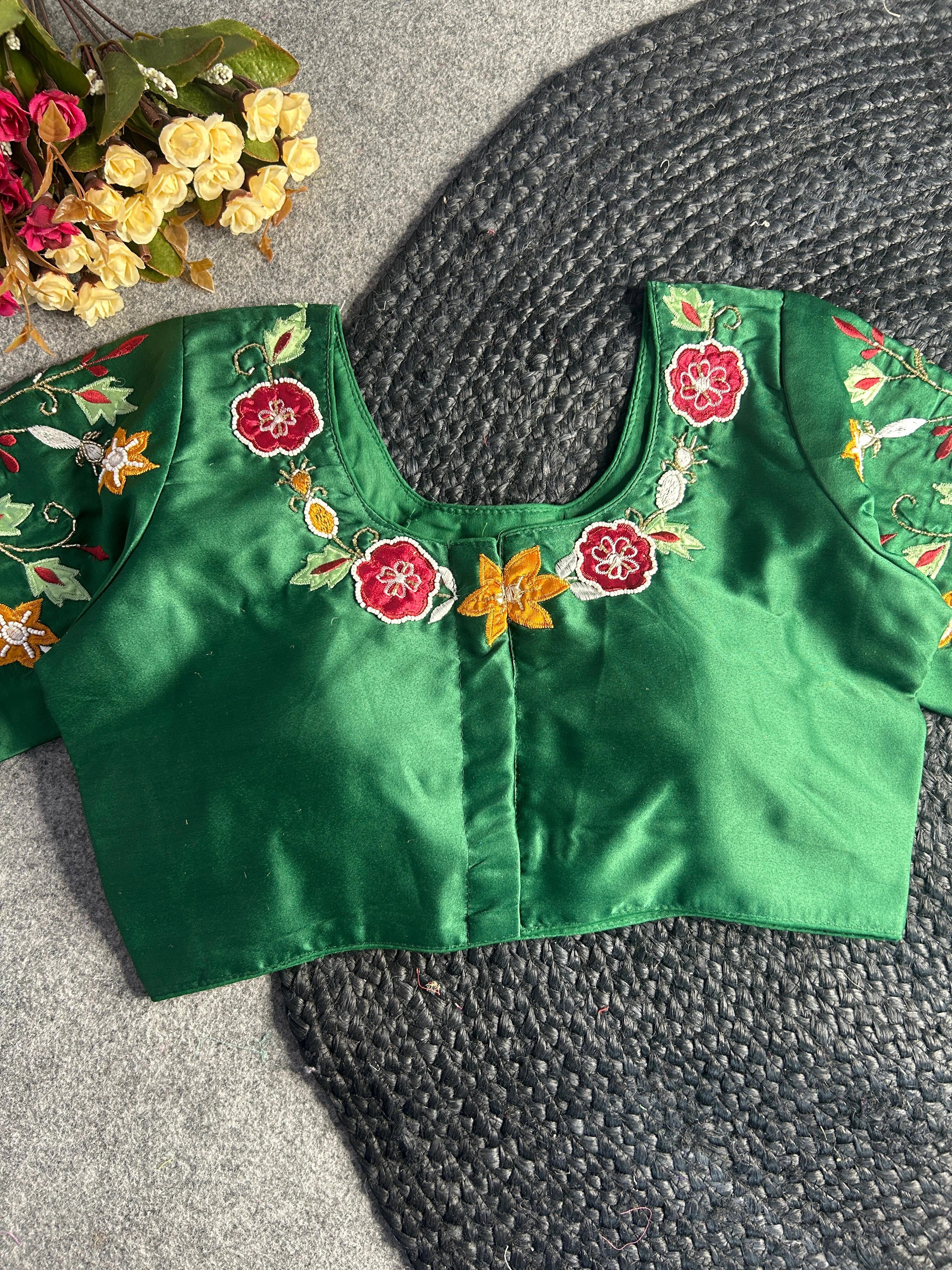 A back-opening version of the green silk blouse, showing a hook-and-eye closure down the center. The embroidery continues along the back neckline with red floral motifs and a central yellow star-shaped flower, framed by delicate vine-like gold stitching.