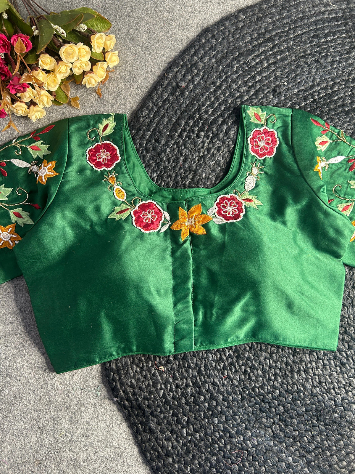 A back-opening version of the green silk blouse, showing a hook-and-eye closure down the center. The embroidery continues along the back neckline with red floral motifs and a central yellow star-shaped flower, framed by delicate vine-like gold stitching.