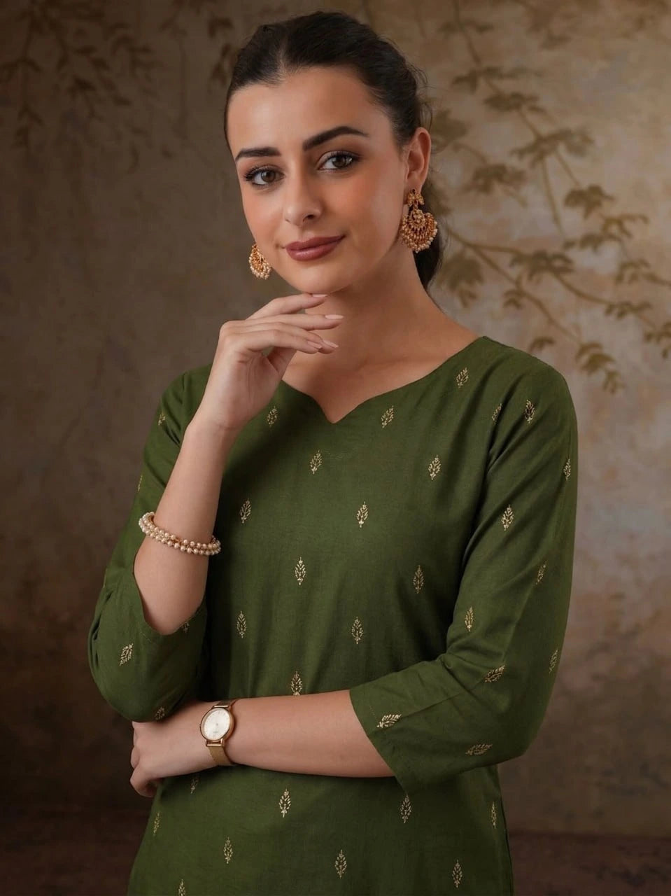 Woman wearing a green traditional outfit with gold jewelry against a textured brown background