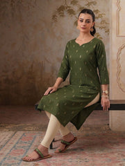 Woman wearing a green kurta with white pants sitting on a decorative rug.