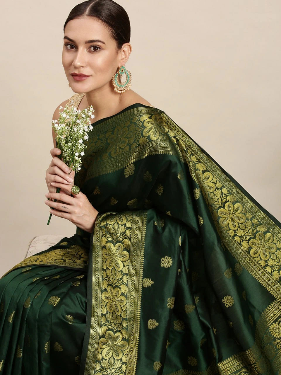 Woman wearing a green saree with gold patterns, holding flowers against a beige background