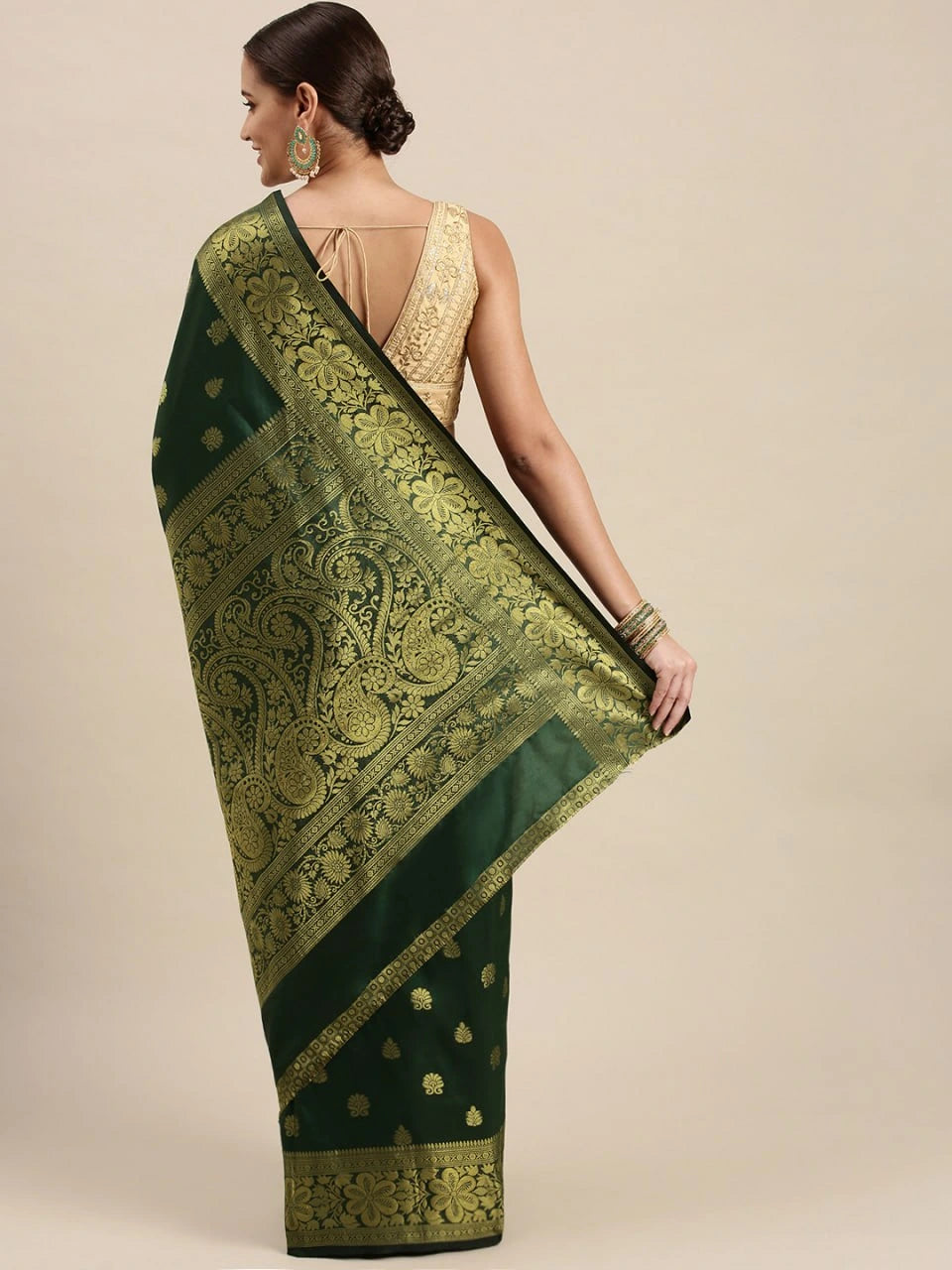 Woman wearing a green saree with gold patterns on a beige background
