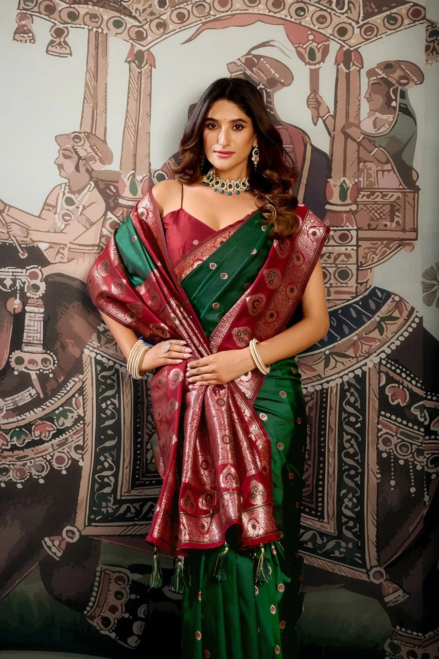 Woman in a red and green saree standing in front of an ornate wall design.
