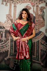 Woman in a red and green saree standing in front of an ornate wall design.