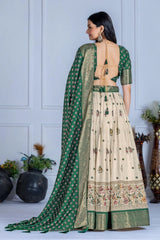 Woman wearing a green and beige traditional outfit with a long green dupatta against a white wall.