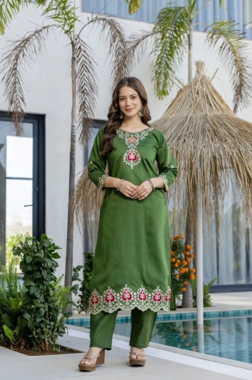 Woman in a green embroidered outfit standing by a pool with palm trees in the background