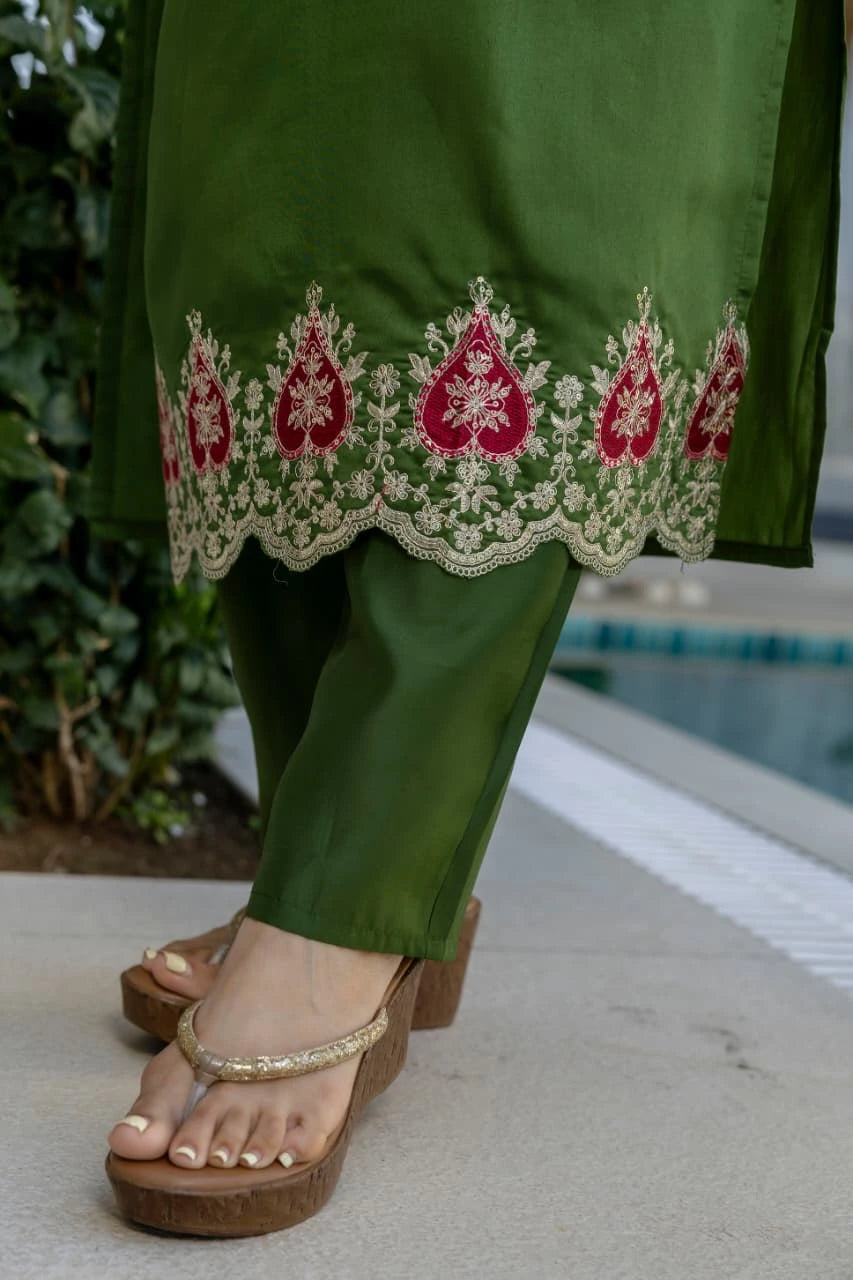 Green embroidered pants with a sandal on a neutral background