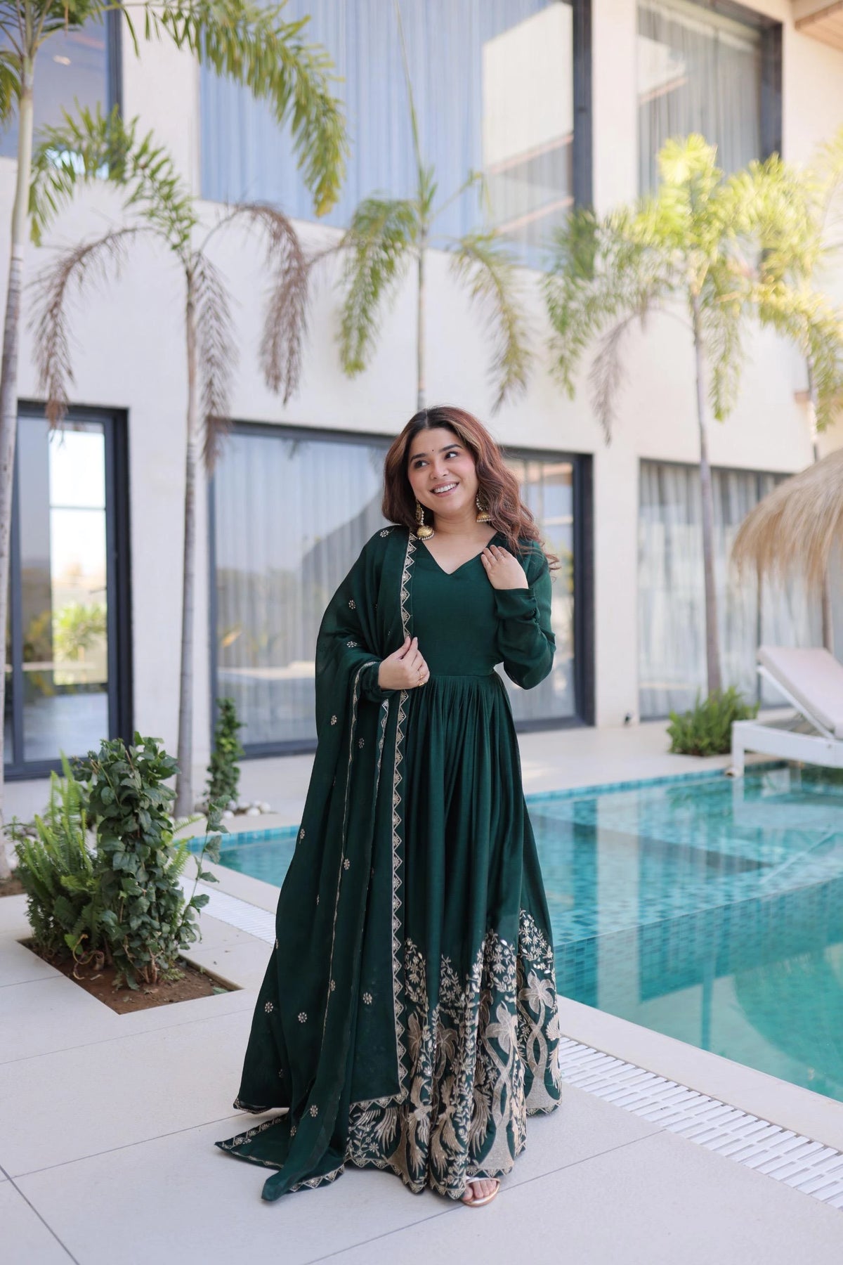 Woman in a green dress standing by a pool with a modern building in the background