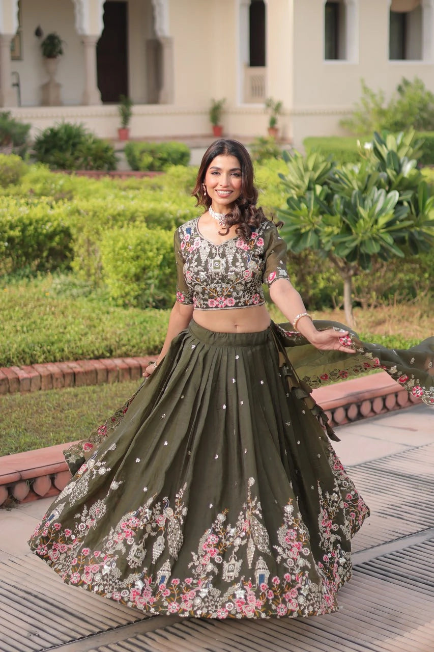 Woman in a floral top and green skirt with embroidery standing in a garden.