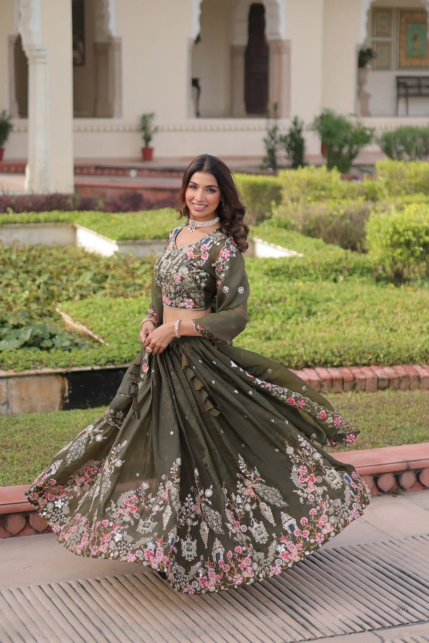Woman in a green floral embroidered traditional outfit standing in a garden.