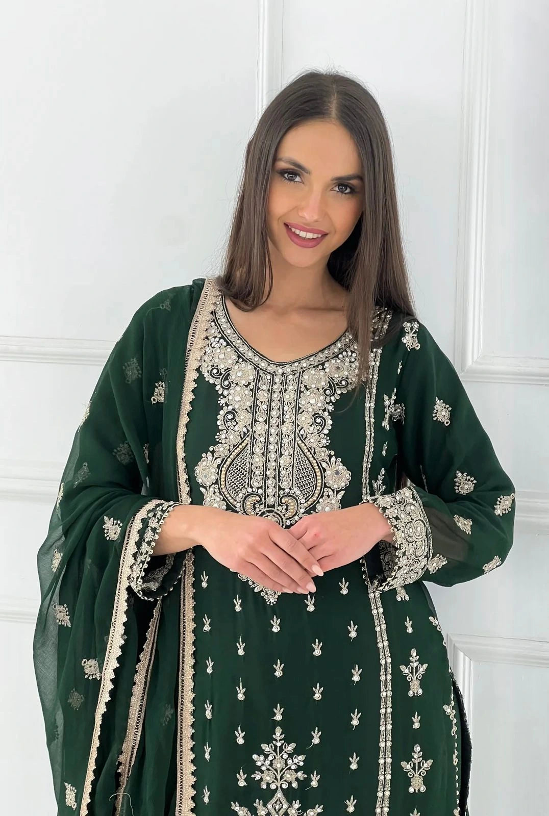 Woman wearing a green embroidered traditional outfit against a white wall