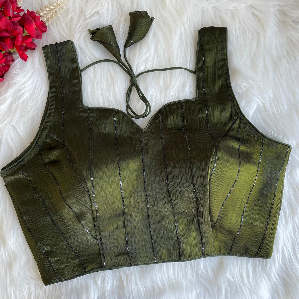 Green crop top with thin straps on a white fluffy surface with red flowers.