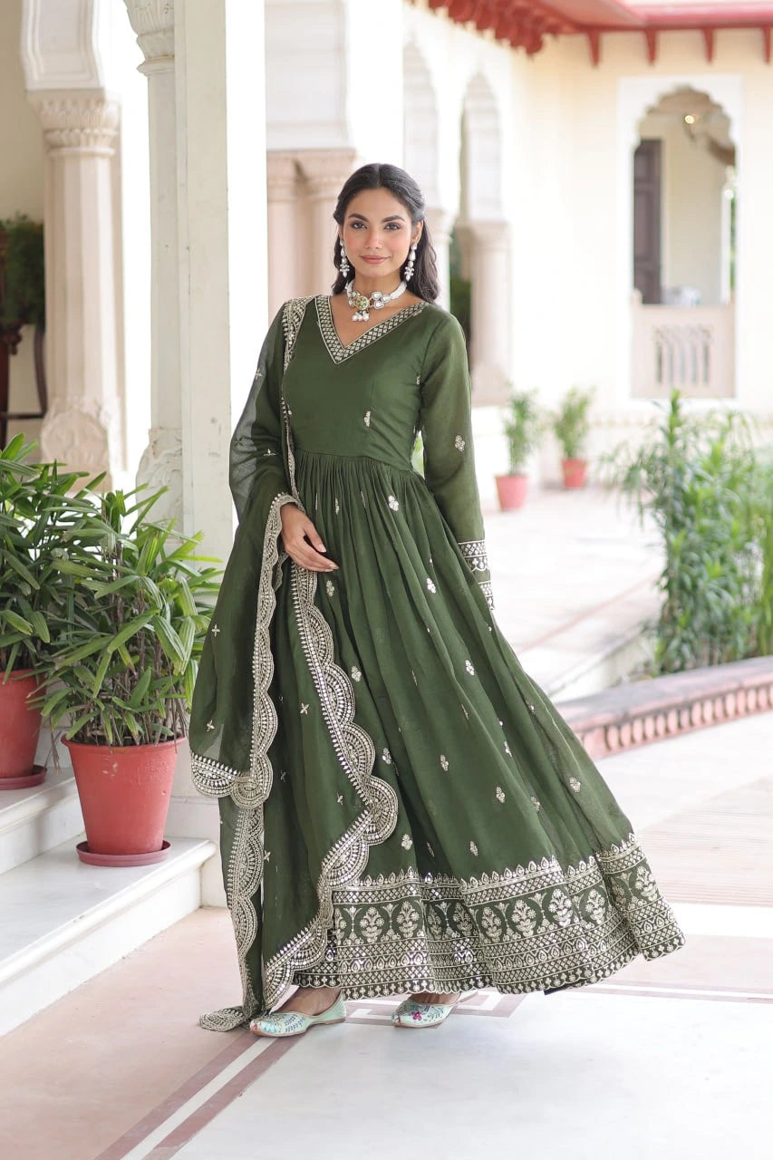 Woman in a green traditional outfit with white embroidery standing in a decorative setting.