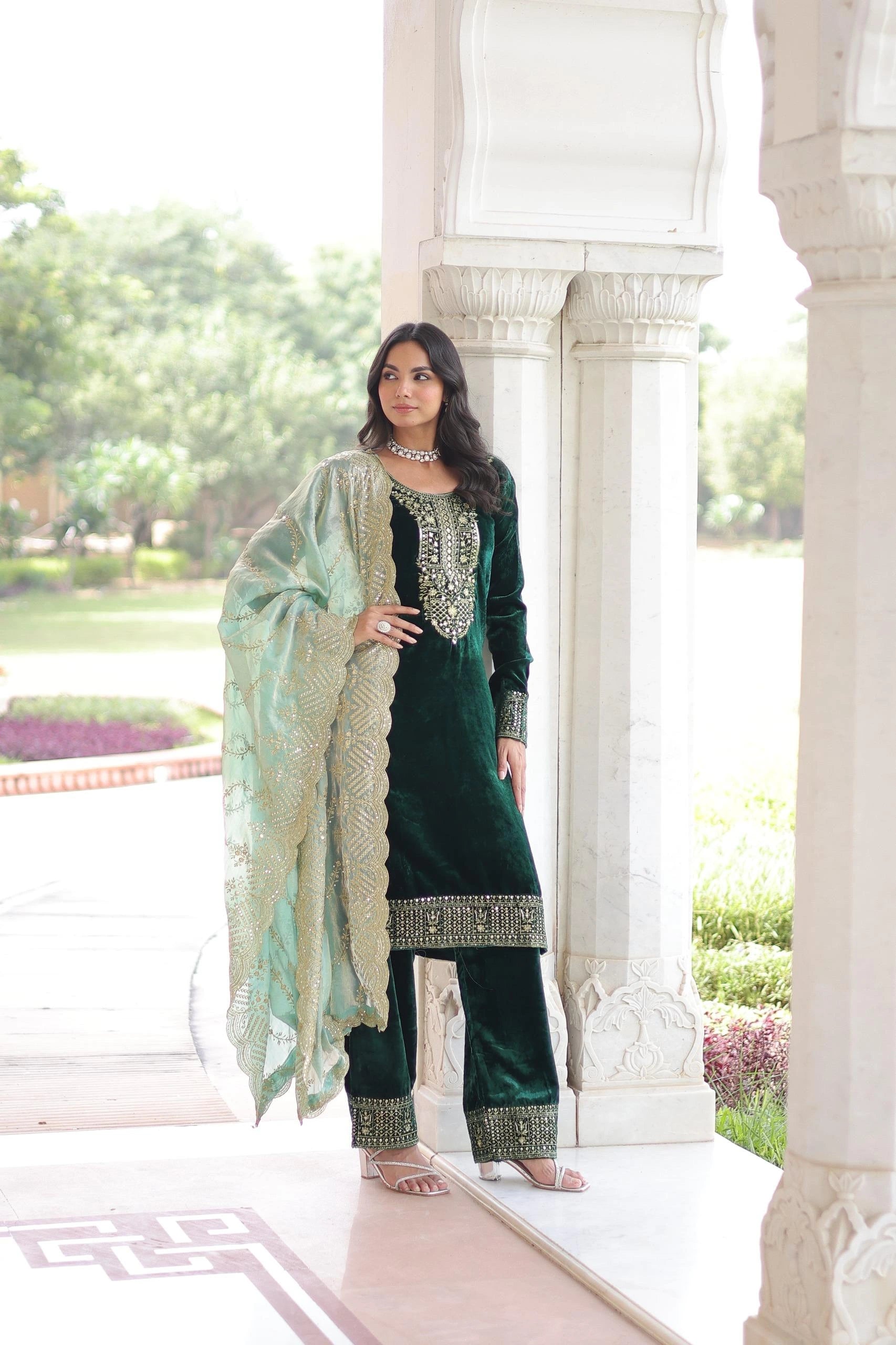 Traditional blue velvet suit with intricate gold detailing and a flowy dupatta, styled with statement jewelry in a palace-like backdrop.