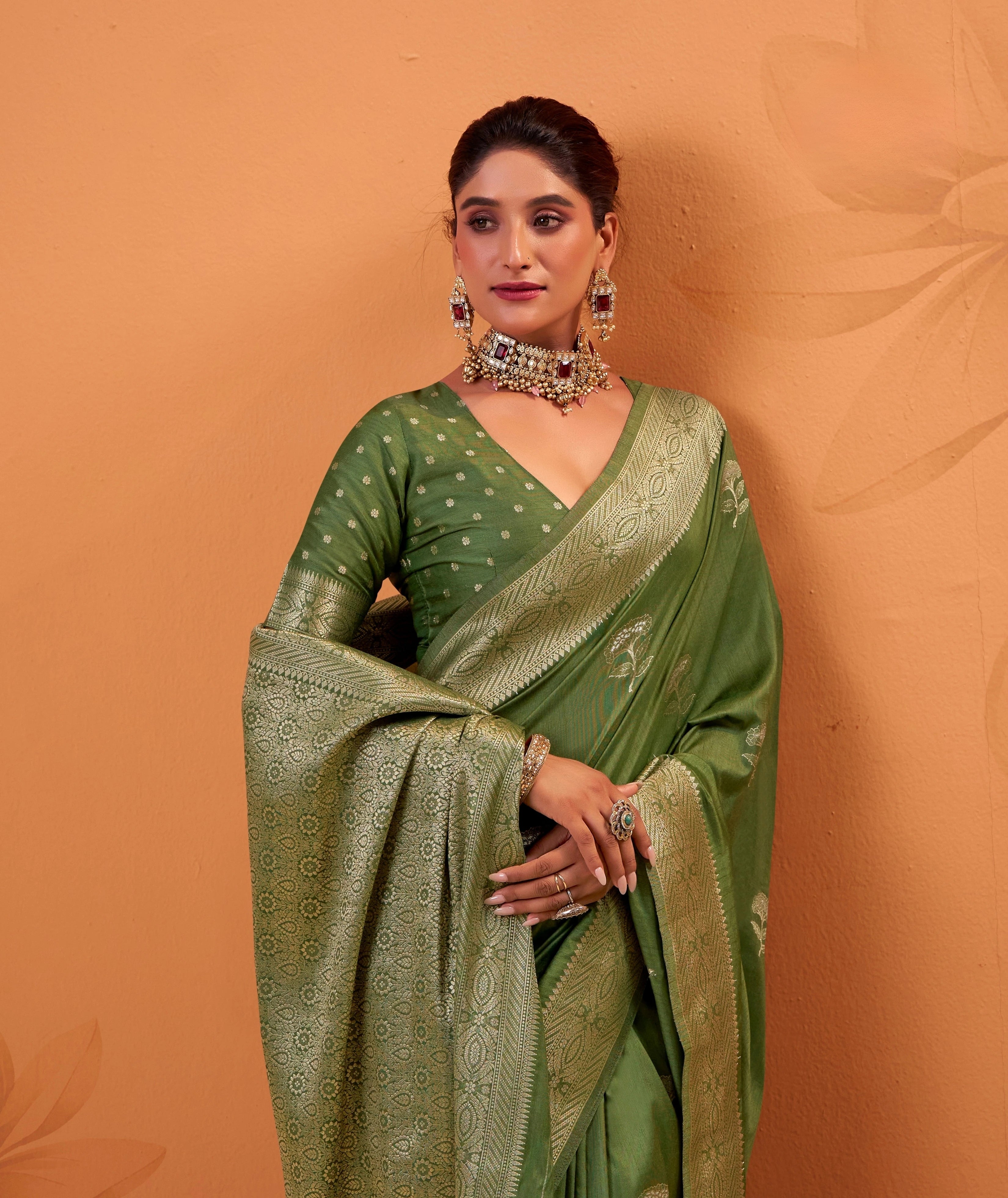 Woman wearing a green saree with a matching blouse against an orange background
