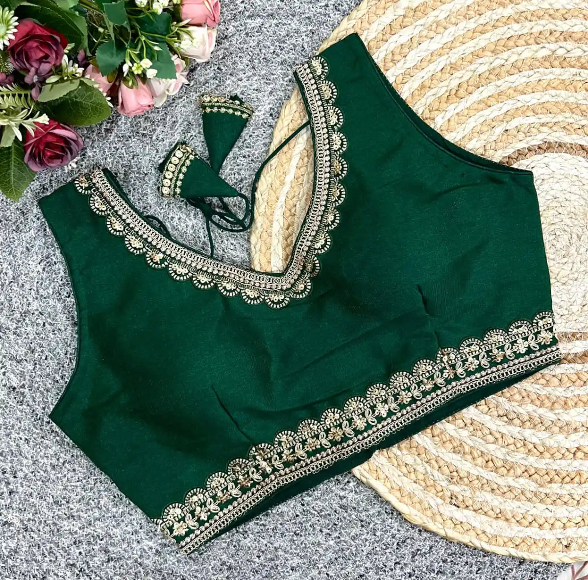 Green blouse with intricate white embroidery on a textured surface with flowers.