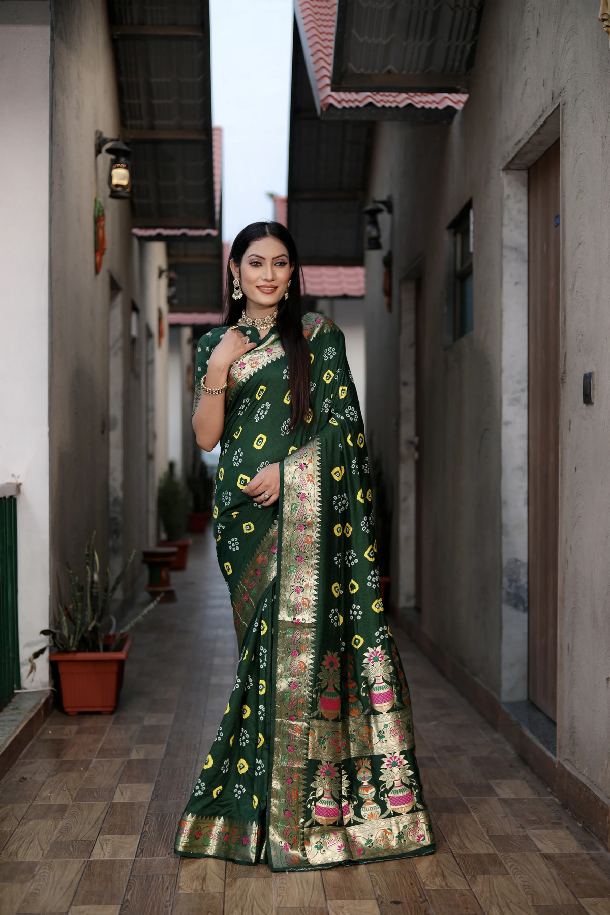Woman in a green saree with floral patterns standing in a narrow alleyway.