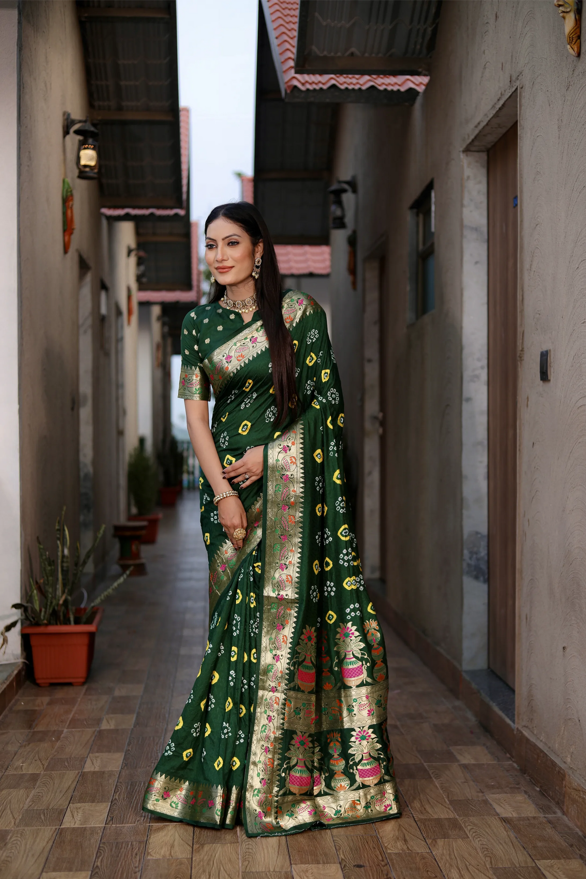 Woman in a green saree with floral patterns standing in a narrow alleyway.