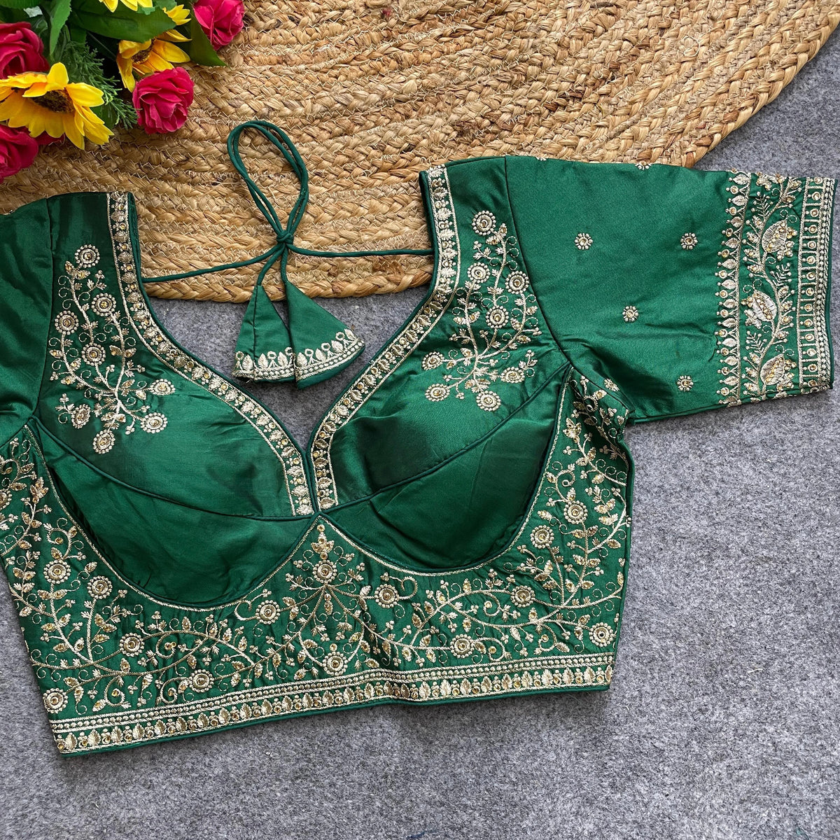 Green embroidered blouse on a textured surface with flowers in the background
