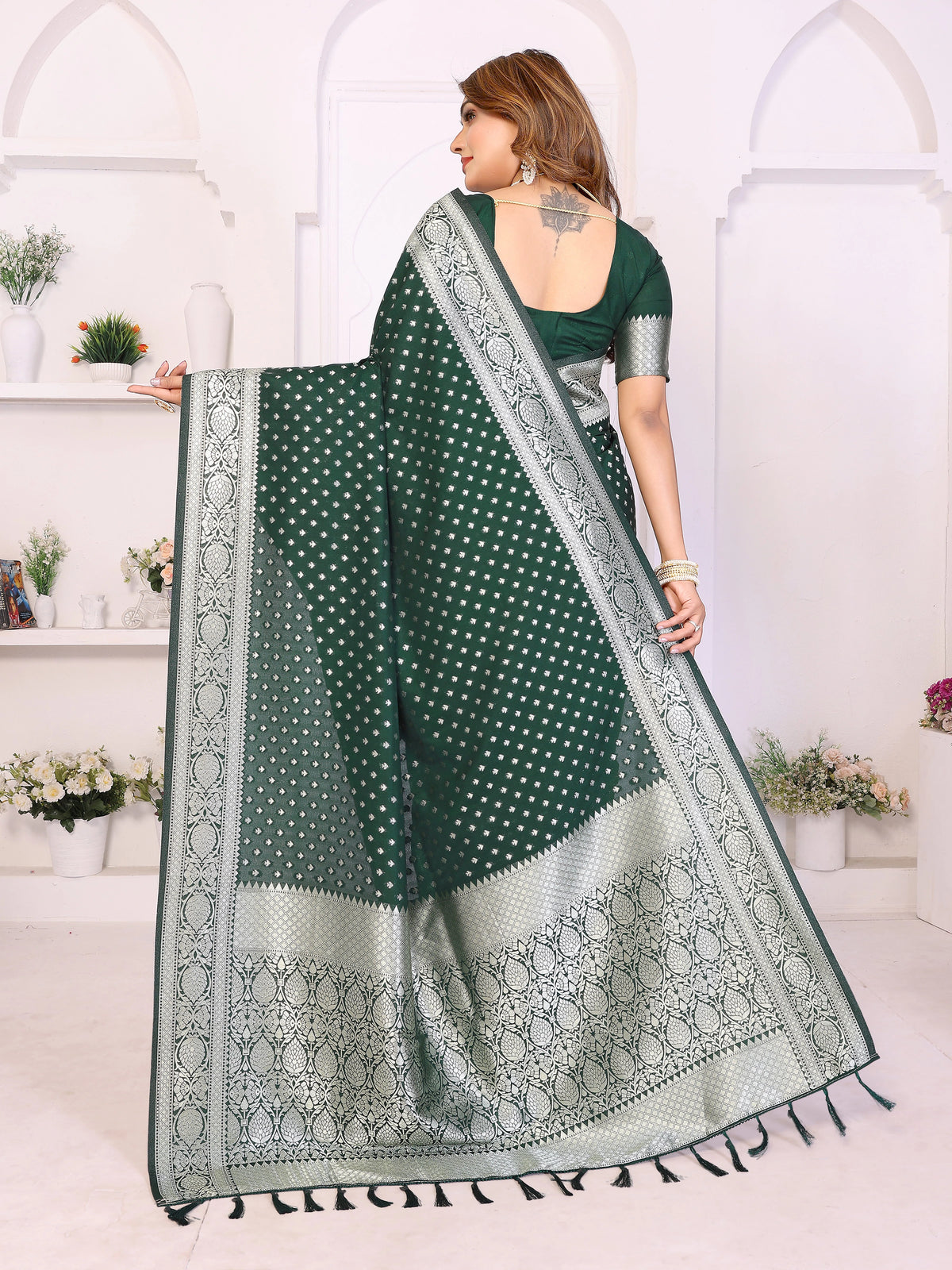 Woman holding a green saree with white patterns in a white room.