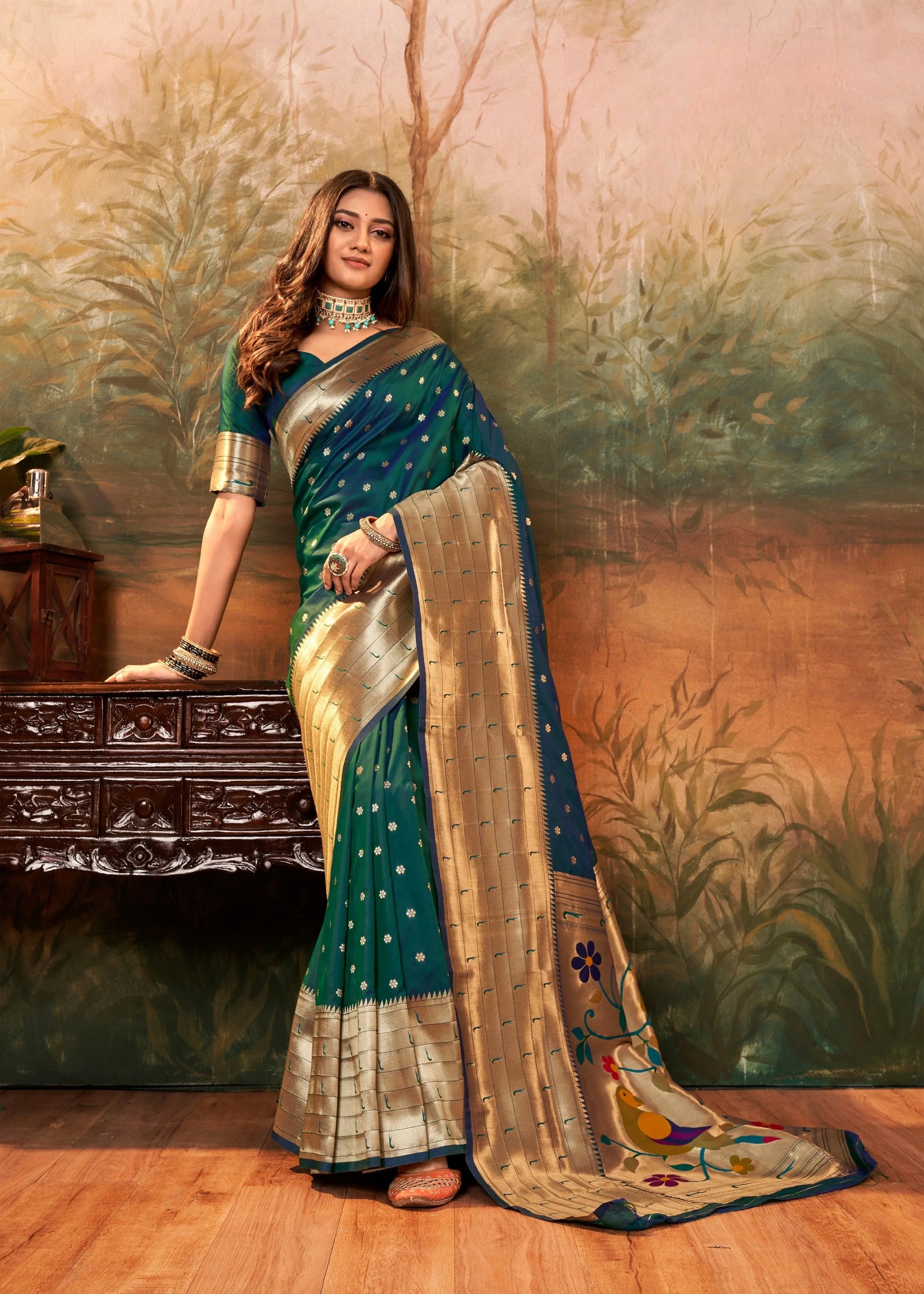 Woman in a traditional saree standing in front of a decorative wall.
