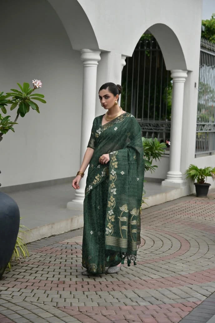 Woman in a green saree standing in an outdoor setting with columns and plants.