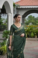 Woman in a green saree with floral patterns standing outdoors.