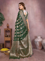 Woman wearing a green saree with a pattern, standing against a pinkish-beige background.