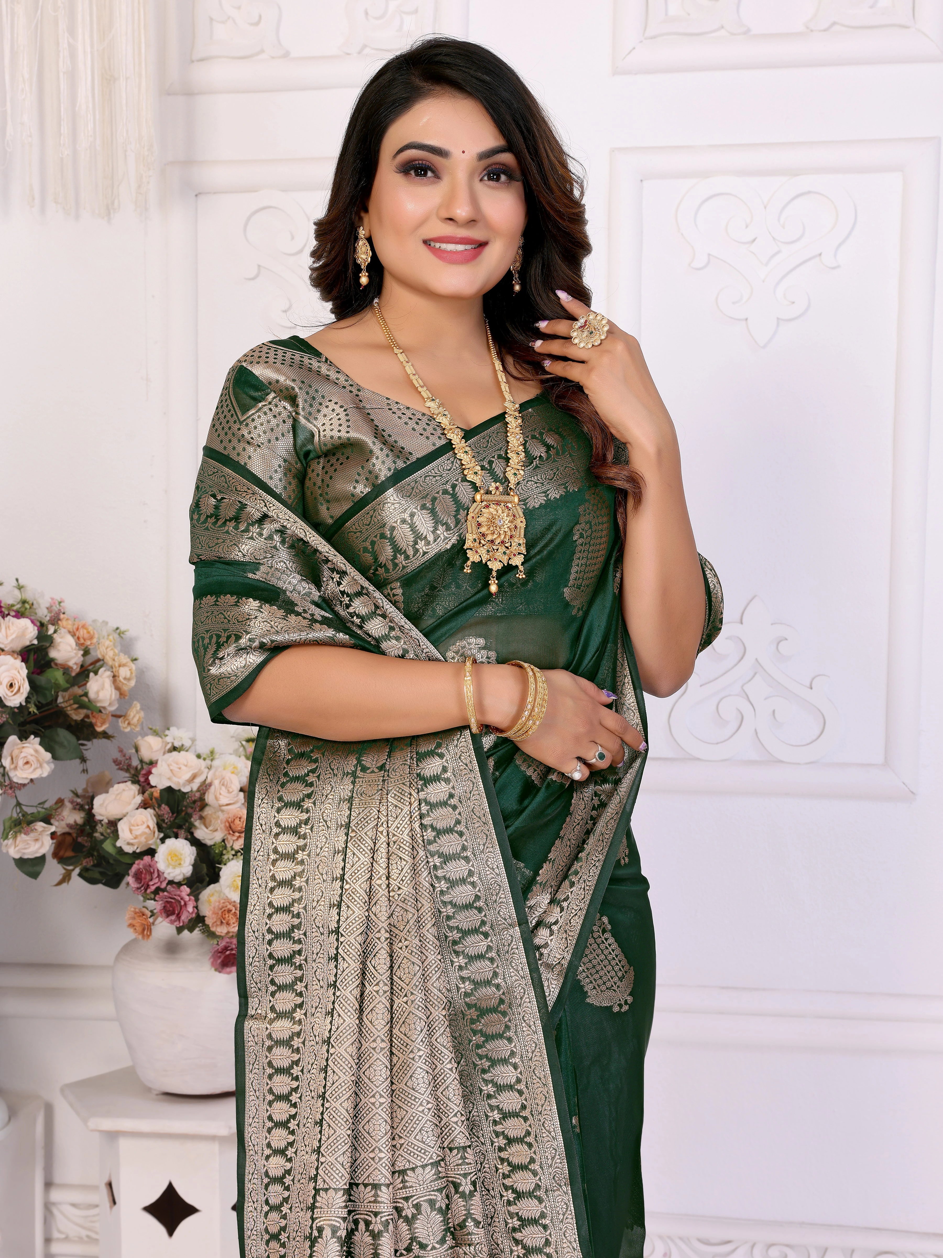 Woman in a green saree with gold patterns against a white decorative wall.