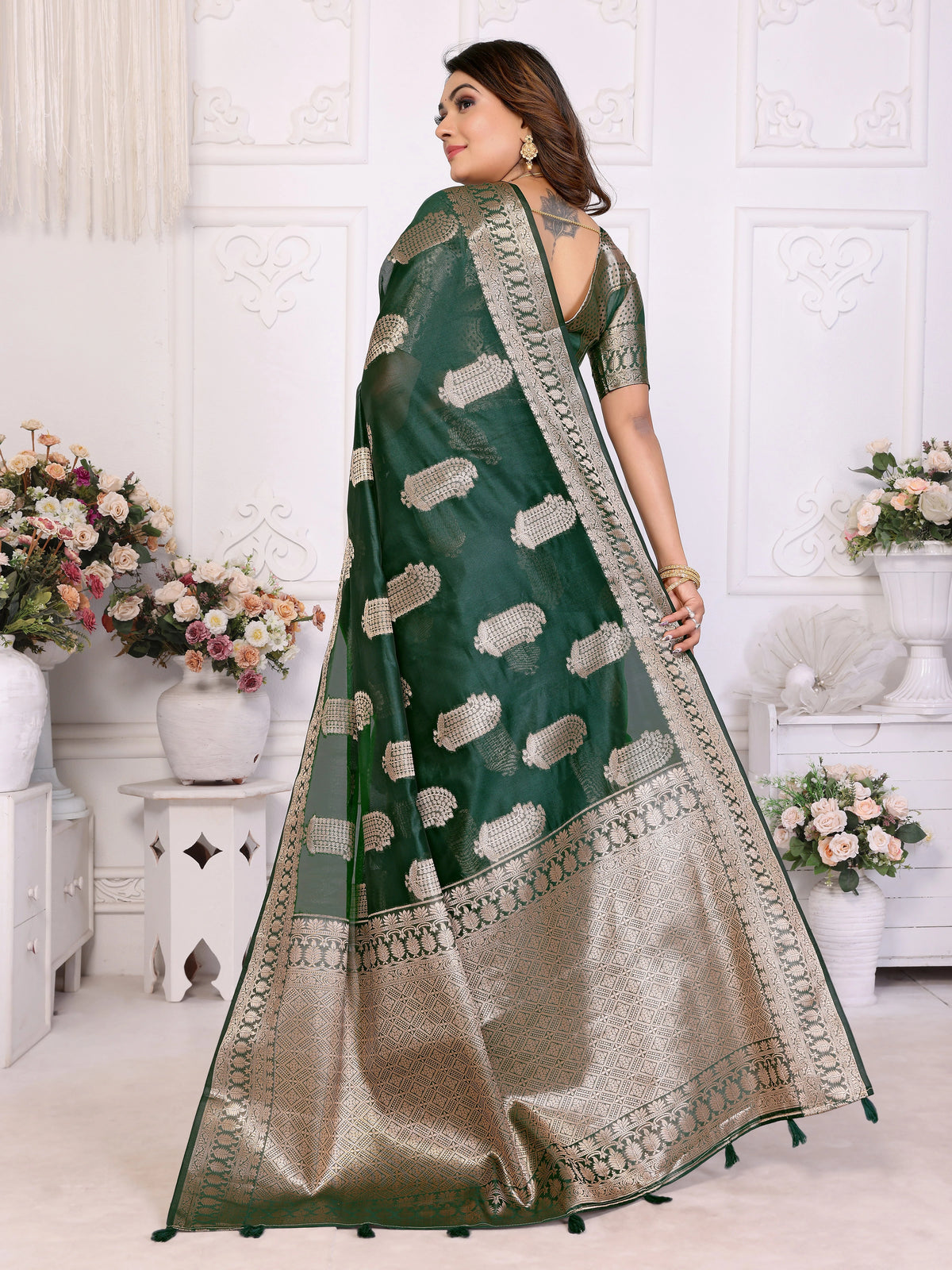 Woman wearing a green and beige saree with floral decorations in the background