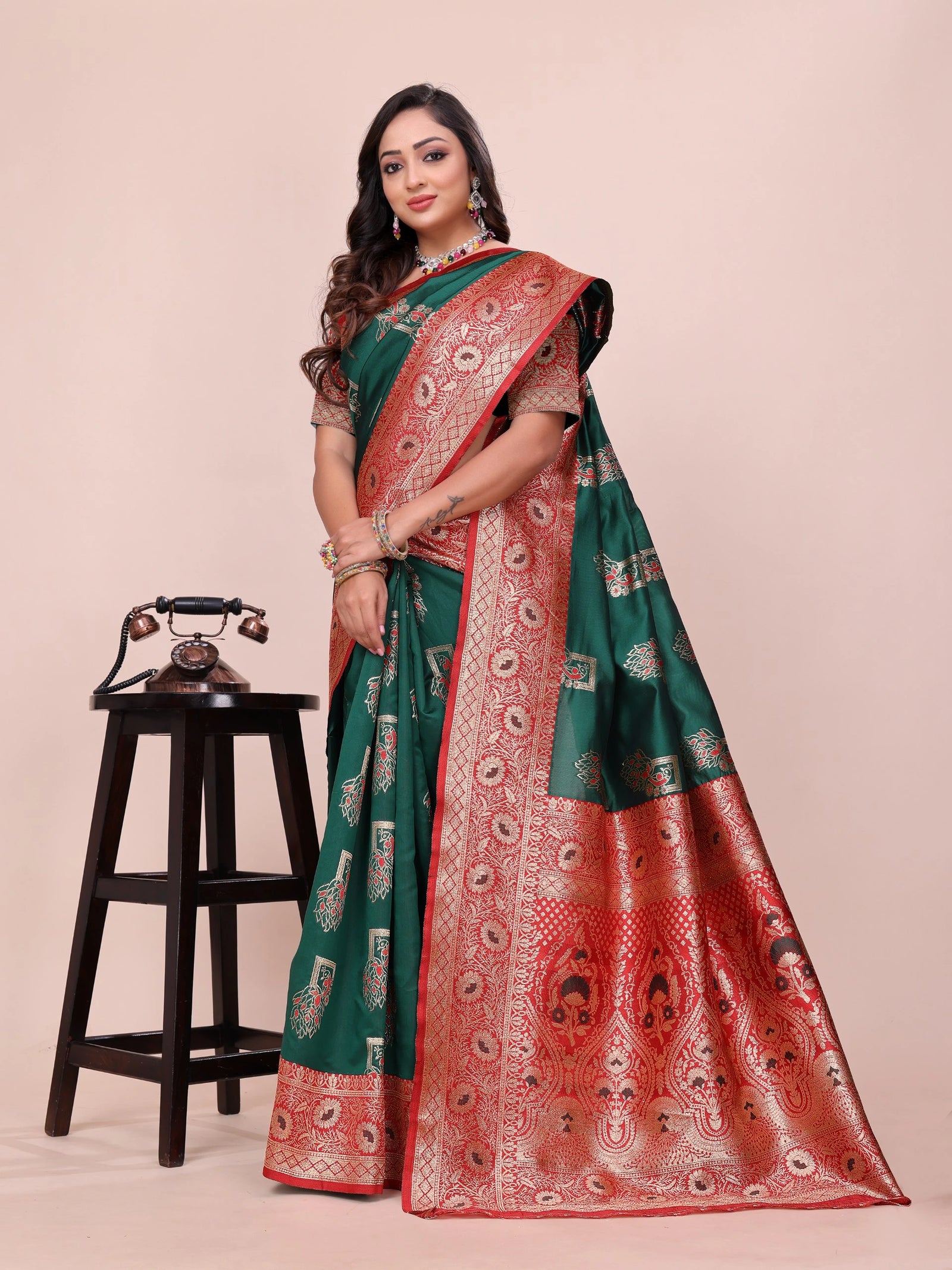 Woman wearing a green and red saree with a vintage phone on a stool in the background
