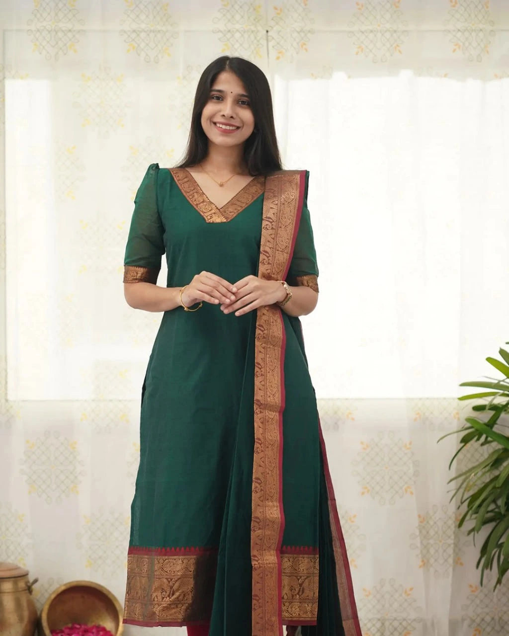 Woman wearing a green traditional outfit with a decorative border indoors.