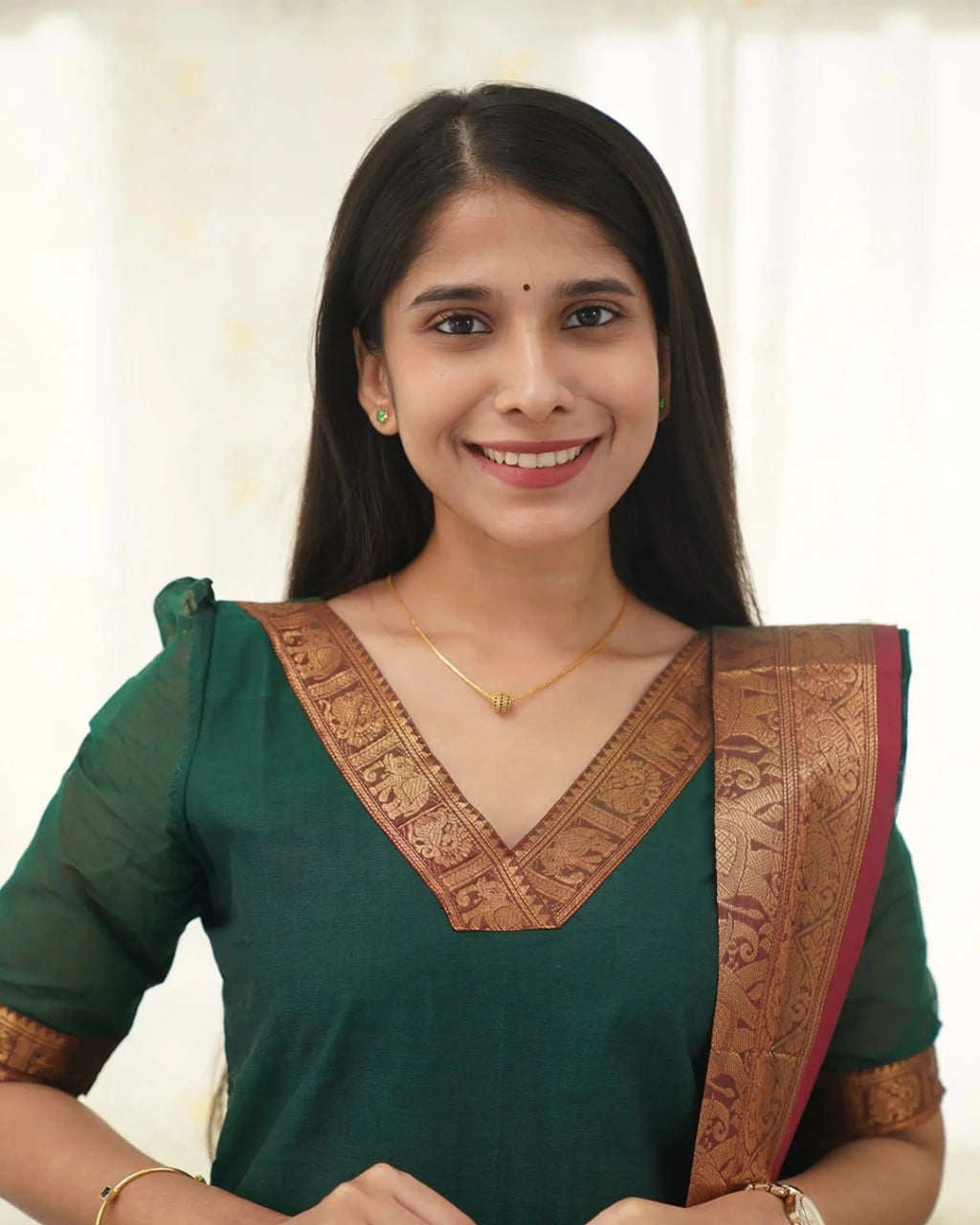 Woman wearing a green saree with gold border against a white background