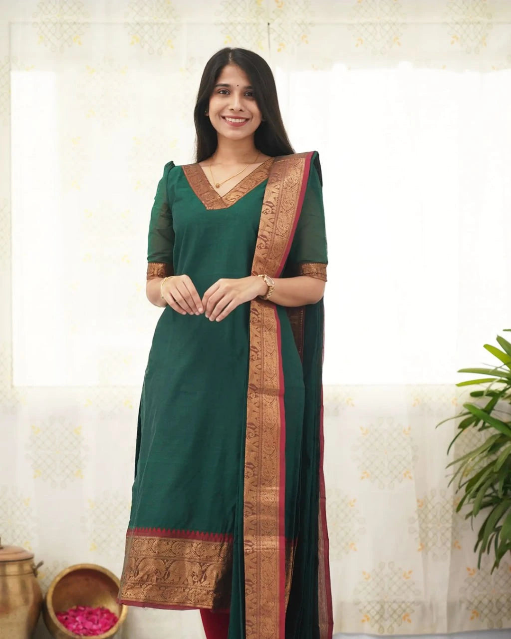 Woman wearing a green saree with a gold border against a light background