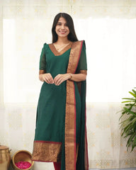 Woman wearing a green saree with a gold border against a light background