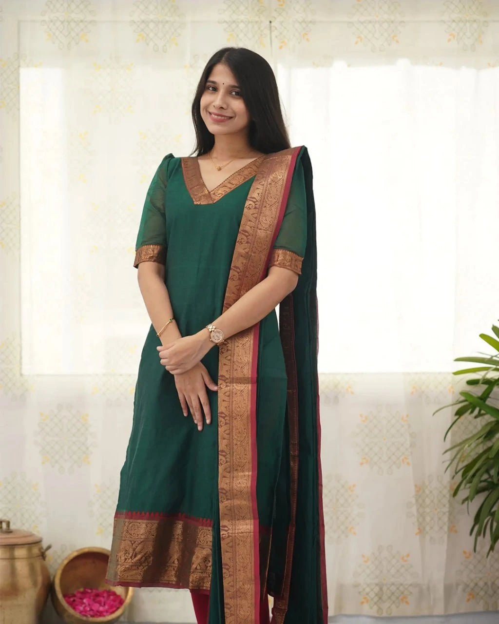 Woman wearing a green saree with a brown border indoors.