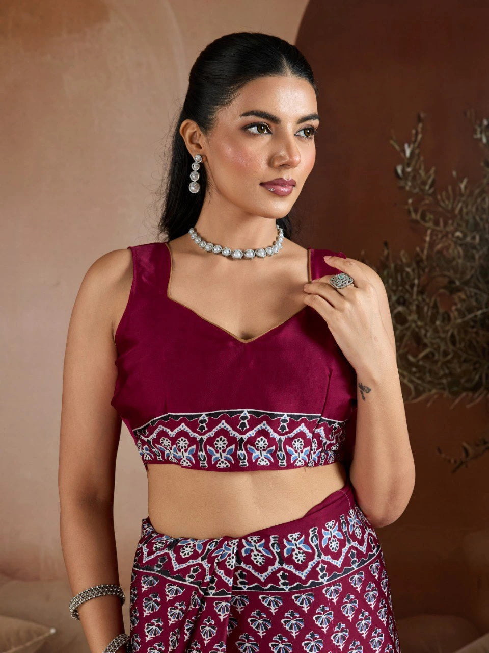 Woman wearing a maroon traditional outfit with intricate patterns against a neutral background