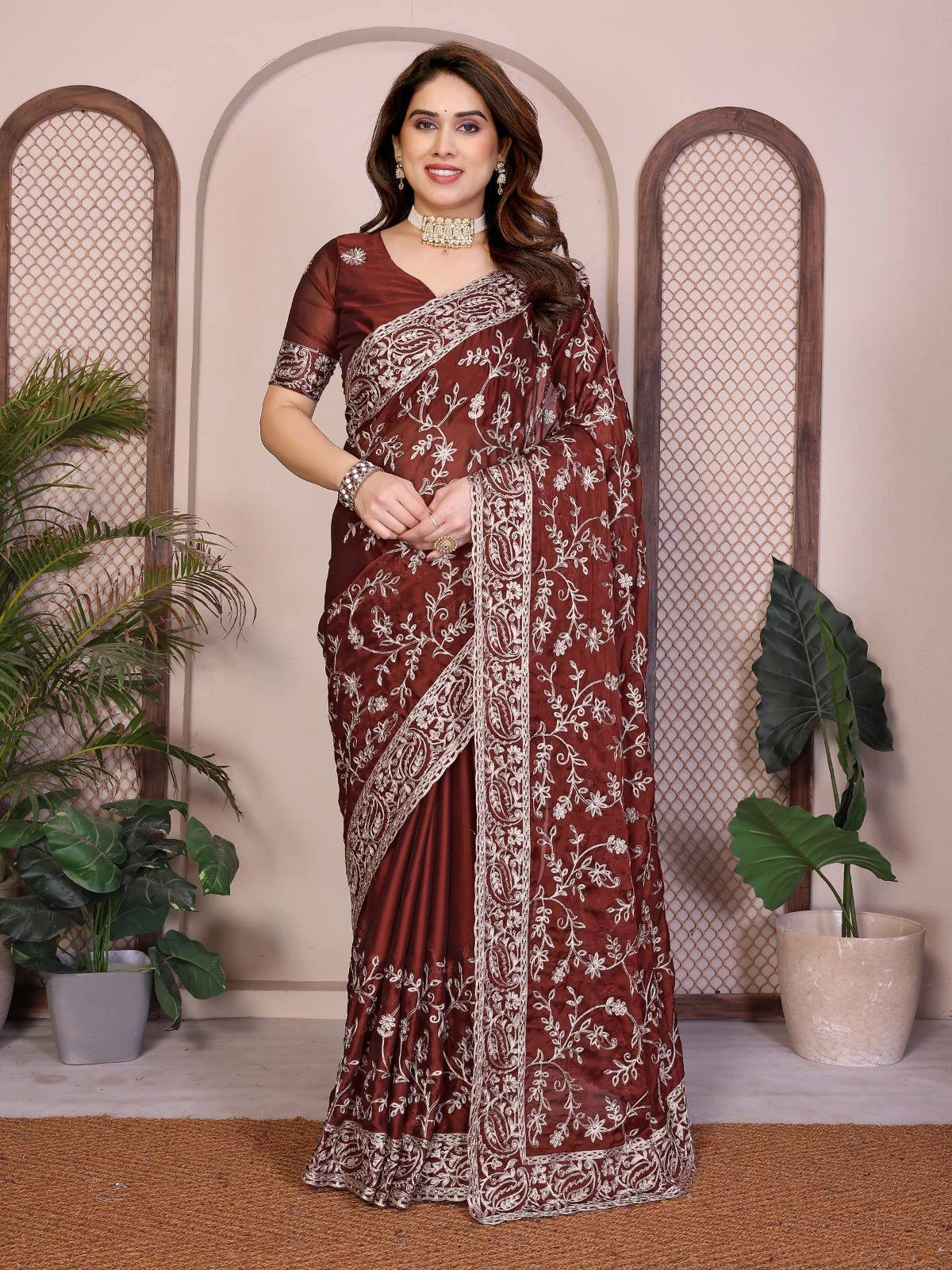 Woman wearing a maroon saree with white patterns in a decorative setting with plants.