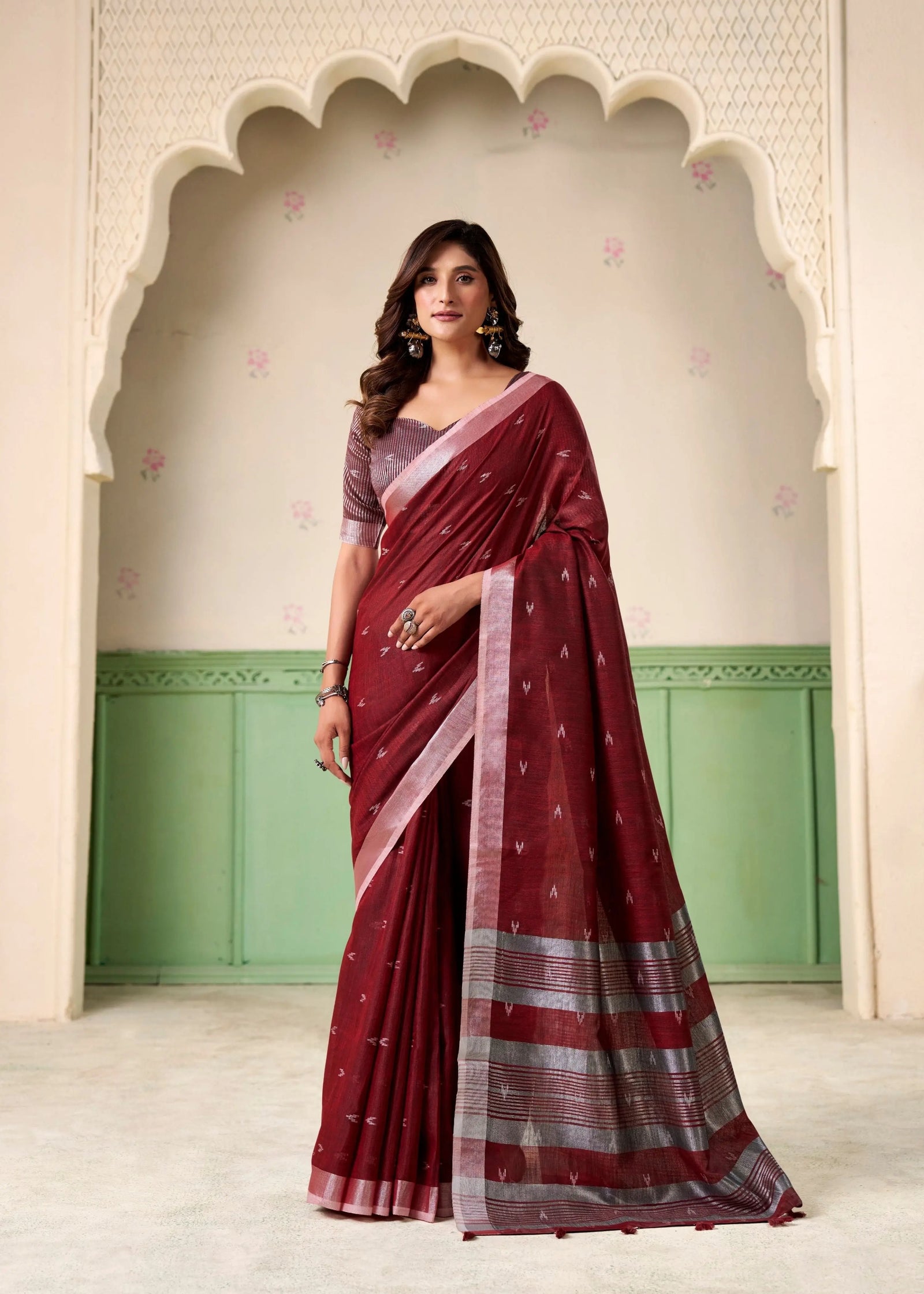 Woman wearing a maroon saree with a green and beige background