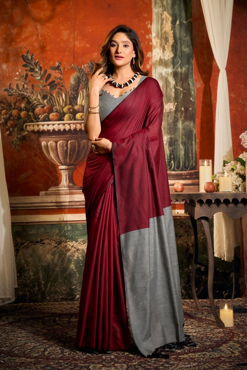 Woman in a maroon and gray saree standing in an ornate room with decorative elements.